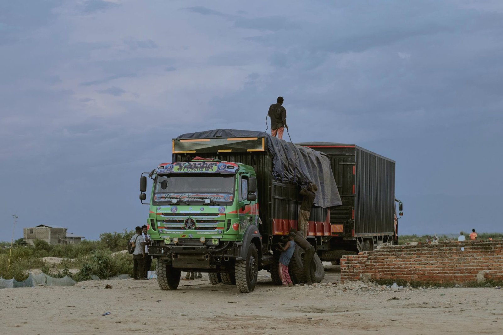A truck with a sheeted load, a man standing on top of it.