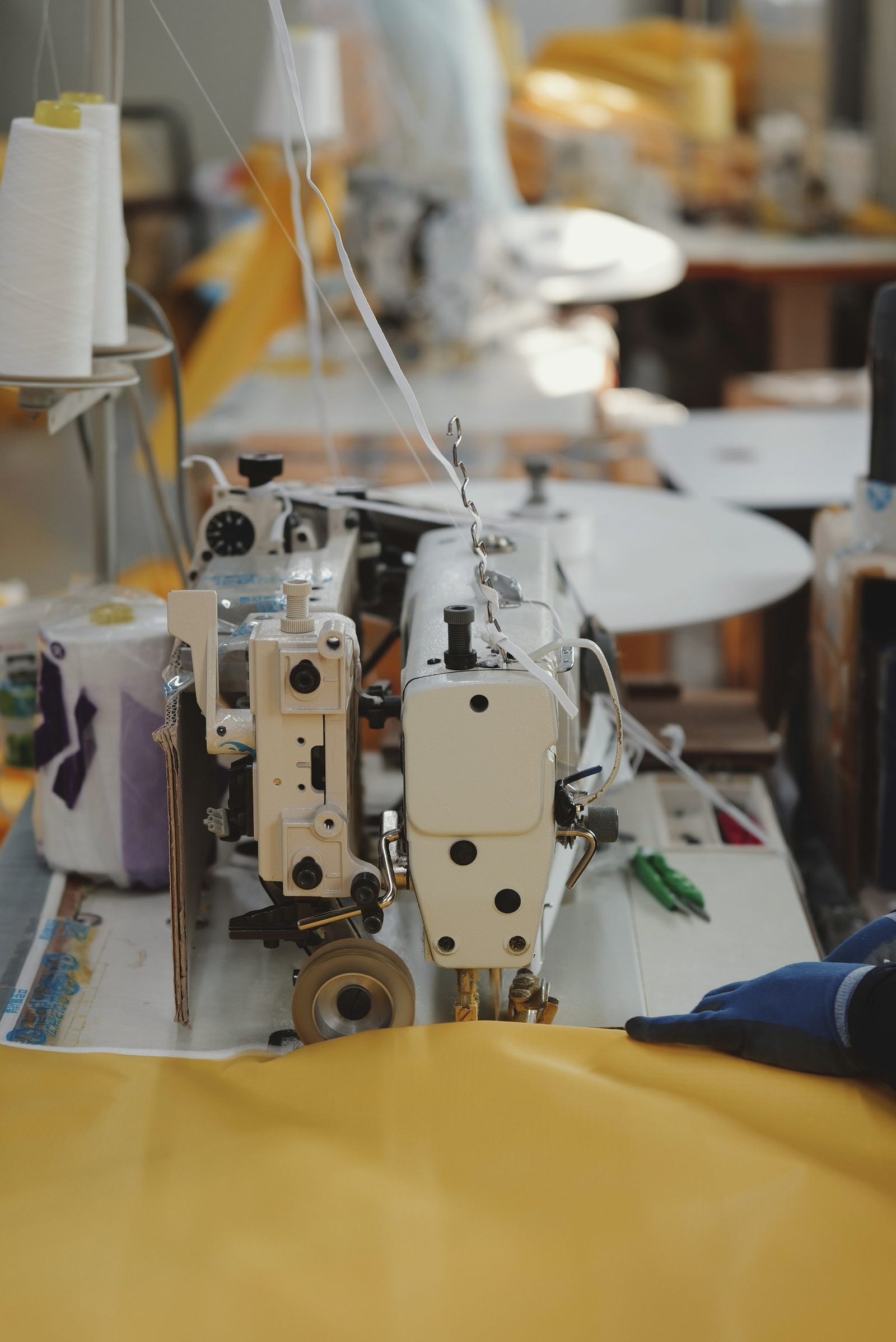 An industrial sewing machine stitching heavy yellow coated fabric.